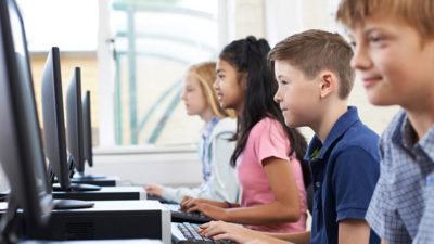 Tre elever sitter på rad och skriver på datorer.