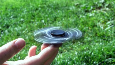 En fidget spinner snurrar på ett finger mot bakgrund av grönt gräs.