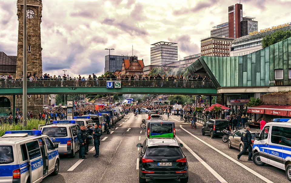 Väg i Hamburg med många polisbilar. Längre bort på vägen är det många människor som protesterar.