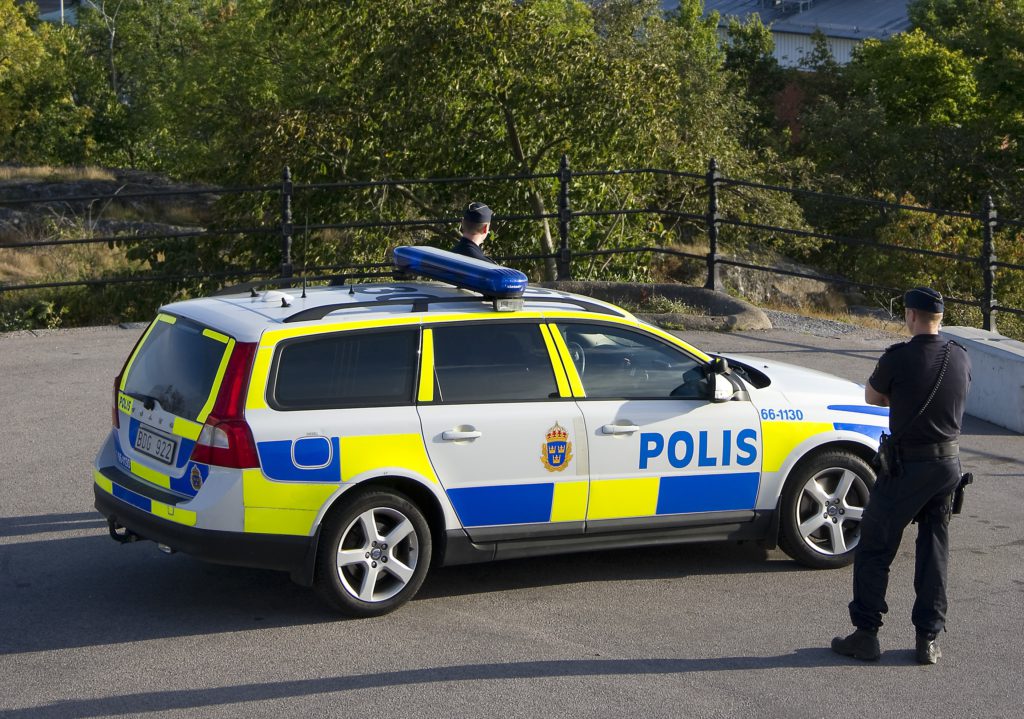 Två poliser står vid en polisbil.