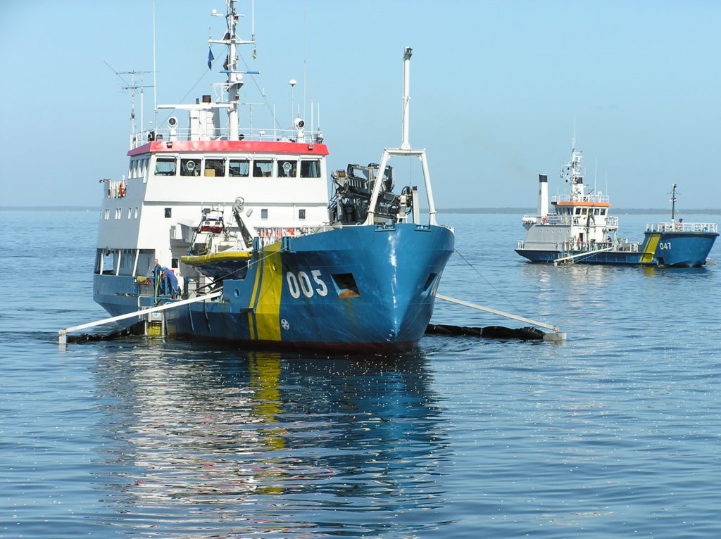 Ett av Kustbevakningens fartyg som kan bogsera båtar. Det är ett medelstort fartyg med ett blått däck. I högra kanten av bilden syns en till båt som är Kustbevakningens.