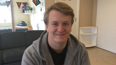 En person med grå munkjacka ler in i kameran.