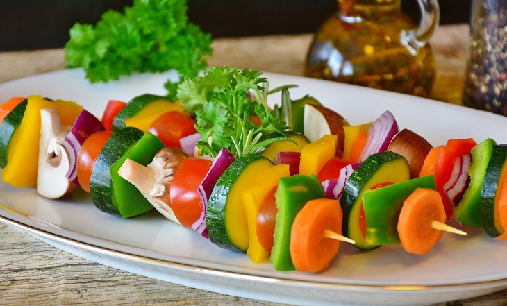 Några grillspett ligger på en tallrik. På spetten sitter det massa olika bitar av grönsaker, som morötter, paprika, svamp, lök och zucchini.