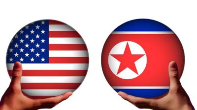 Två händer håller i varsin kula. Den ena kulan har USA:s flagga, med röda och vita ränder och vita stjärnor på en blå bakgrund i ena hörnet. Den andra kulan har Nordkoreas flagga. Den har en bred röd rand i mitten, blåa kanter och en vit cirkel med en röd stjärna i.