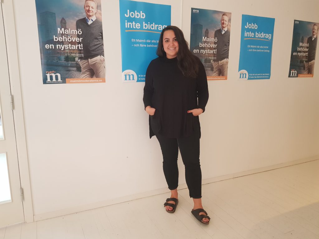 Noria på sitt kontor, framför affischer med Moderaternas logga och andra budskap.